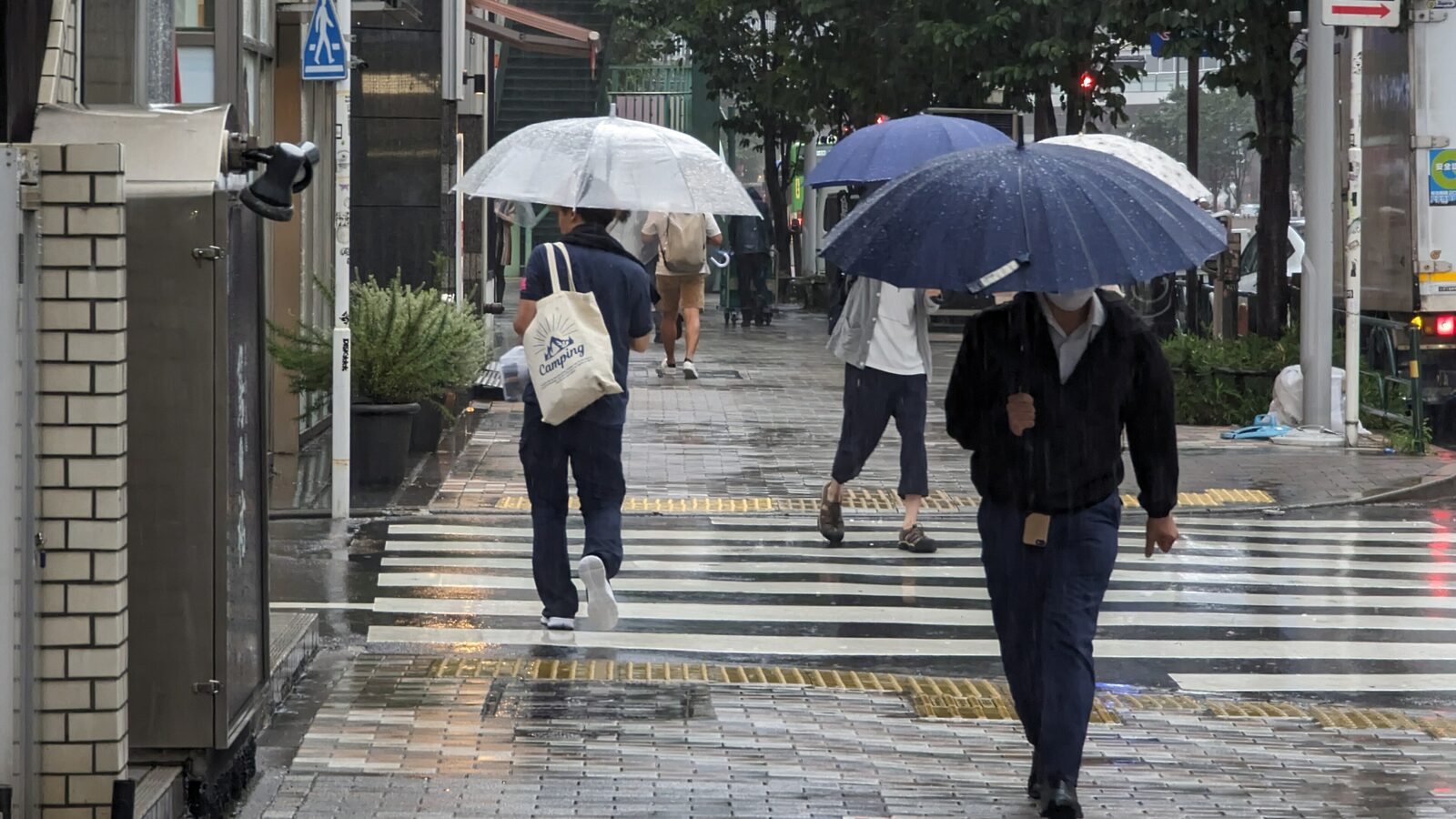 台風の雨の中、傘をさして横断歩道を渡る渋谷の人々。